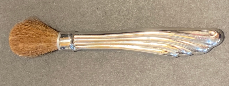 May include: A silver makeup brush with a brown bristle brush head.