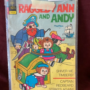 May include: A comic book cover featuring Raggedy Ann and Andy, with the title "Raggedy Ann and Andy" and the tagline "Shiver Me Timbers! Captain Redbeard Strikes Again!" The cover features a pirate with a red beard and a treasure chest.