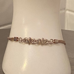 May include: A silver chain bracelet with a unique, interlocking design. The bracelet is made of a delicate chain and features a repeating pattern of linked loops.