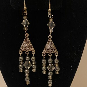 May include: Silver dangle earrings with a triangular charm, clear crystal beads, and black beads.
