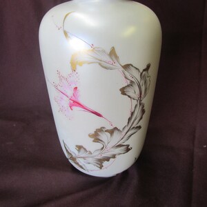 May include: White ceramic vase with a floral design. The vase has a pink and gold floral pattern with leaves and a flower.