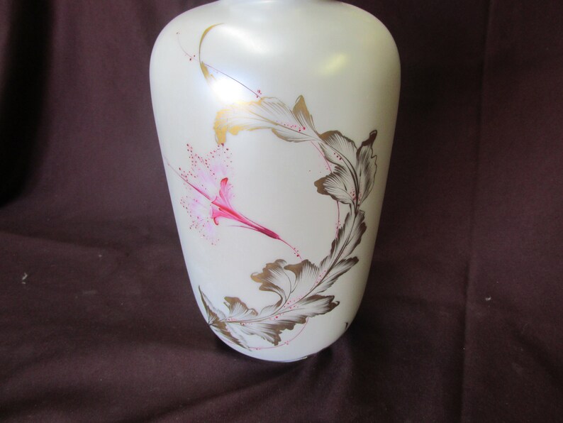May include: White ceramic vase with a floral design. The vase has a pink and gold floral pattern with leaves and a flower.