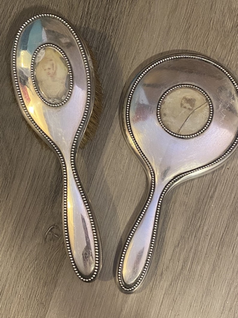 Puede incluir: Un juego de espejo de mano y cepillo para el cabello plateado con un borde de cuentas. Cada pieza presenta un inserto circular con una imagen descolorida de un ni&ntilde;o.