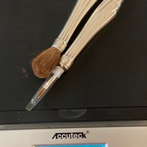 May include: Two silver makeup brushes with decorative handles on a digital scale that reads 29.64 grams.
