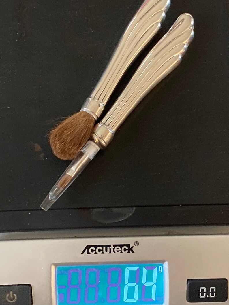 May include: Two silver makeup brushes with decorative handles on a digital scale that reads 29.64 grams.