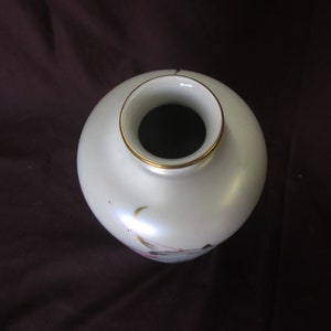 May include: White ceramic vase with a gold rim and delicate floral designs. The vase has a round body and a narrow opening.