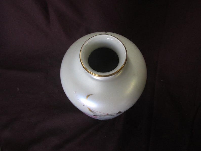 May include: White ceramic vase with a gold rim and delicate floral designs. The vase has a round body and a narrow opening.