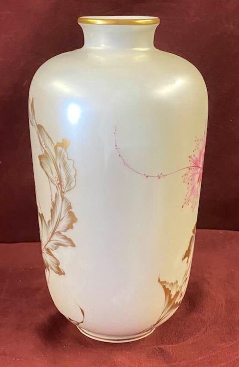 May include: A white ceramic vase with a gold rim and delicate pink and gold floral designs. The vase has a pearlescent finish.