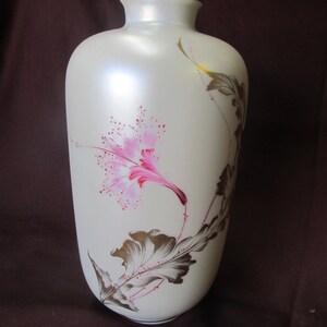 May include: A white ceramic vase with a pink and gold floral design. The vase has a smooth, matte finish and is decorated with a single pink flower and gold leaves.