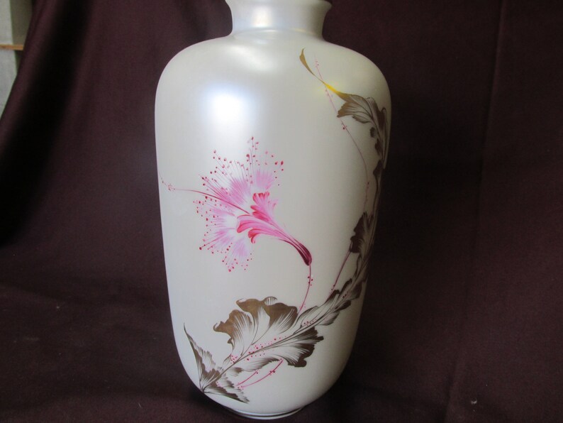 May include: A white ceramic vase with a pink and gold floral design. The vase has a smooth, matte finish and is decorated with a single pink flower and gold leaves.