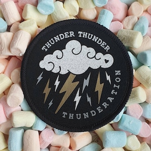 May include: Black fabric patch with a white cloud and gold lightning bolts. The text "THUNDER THUNDERATION" is written around the edge of the patch.