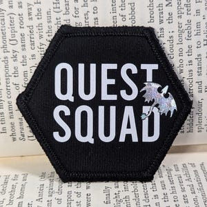 May include: A black hexagonal patch with white text that reads "QUEST SQUAD" and a silver holographic dragon design.
