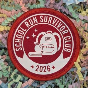 Peut inclure: Un écusson rond rouge avec du texte et des graphiques blancs. Le texte dit "SCHOOL RUN SURVIVOR CLUB" sur le bord, avec "+ 2026 +" en bas. Un sac à dos, une pomme et un livre sont au centre.
