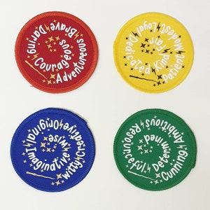 May include: Four round fabric badges with a white spiral design on a coloured background. The badges feature words like "Brave", "Courageous", "Adventurous", "Dedicated", "Kind", "Patient", "Imaginative", "Witty", "Ambitious", "Determined", "Resourceful", "Cunning".