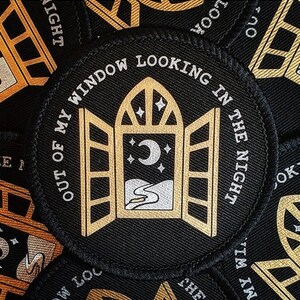 May include: A black embroidered patch with gold thread depicting a window looking out at a crescent moon and stars. The text "Out of my window looking in the night" is written around the window.