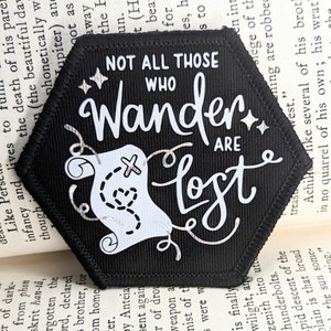May include: Black hexagonal patch with white text and a white compass design. The text reads "Not all those who wander are lost."
