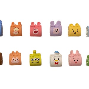 May include: A set of 10 colourful, cartoon character-themed cake roll charms. Each charm features a different character, including Stitch, Tigger, Piglet, Mickey Mouse, Donald Duck, and more.
