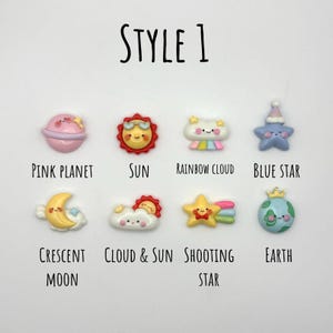 May include: A collection of colorful, cartoon-style celestial-themed embellishments. The designs include a pink planet, sun, rainbow cloud, blue star, crescent moon, cloud and sun, shooting star, and earth. The text "STYLE 1" is at the top.