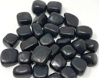 May include: A pile of black tumbled obsidian stones. The stones are smooth and polished, and they have a dark, almost black color.