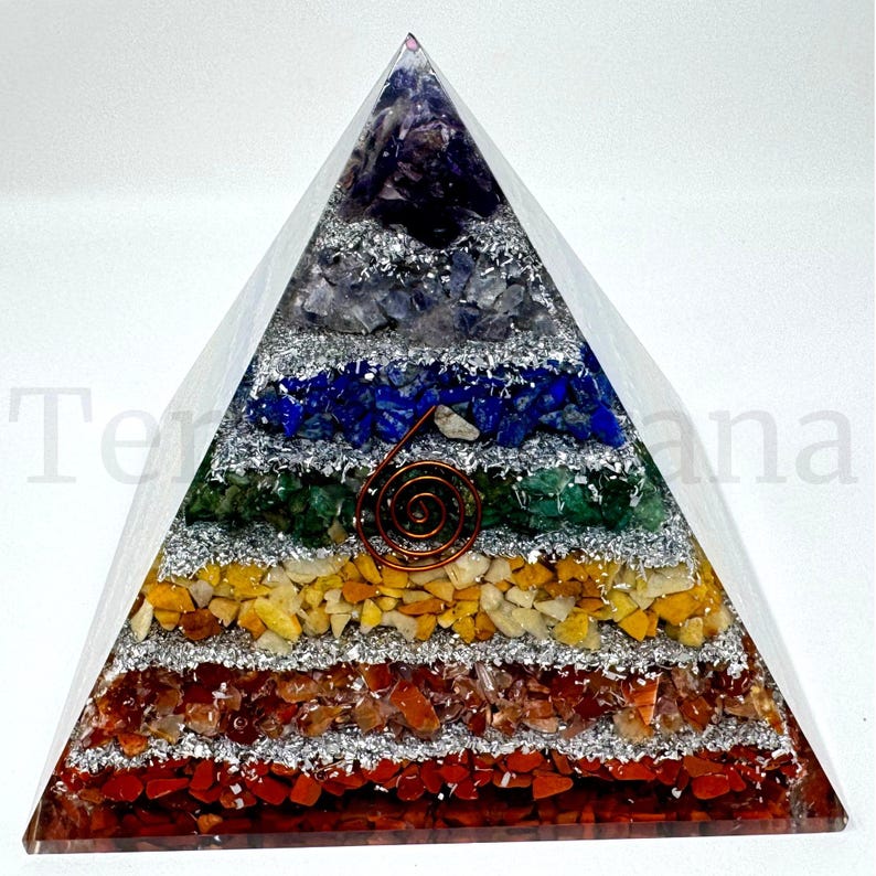 May include: A layered pyramid sculpture with a clear resin exterior. The layers are composed of various colored stones, including red, orange, yellow, green, blue, and purple. A copper spiral is embedded in the center. The pyramid is on a white background.