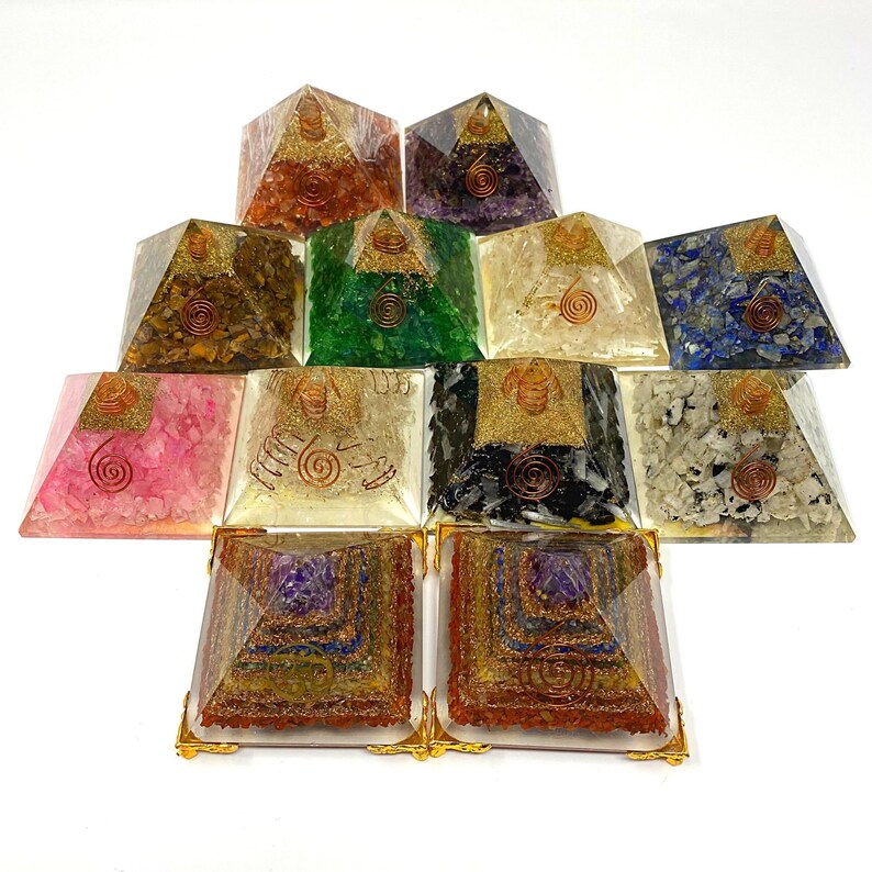 May include: A collection of colorful crystal pyramids. Each pyramid features a unique combination of colors and textures, with a copper spiral at the top. The pyramids are arranged on a white surface, showcasing their variety.