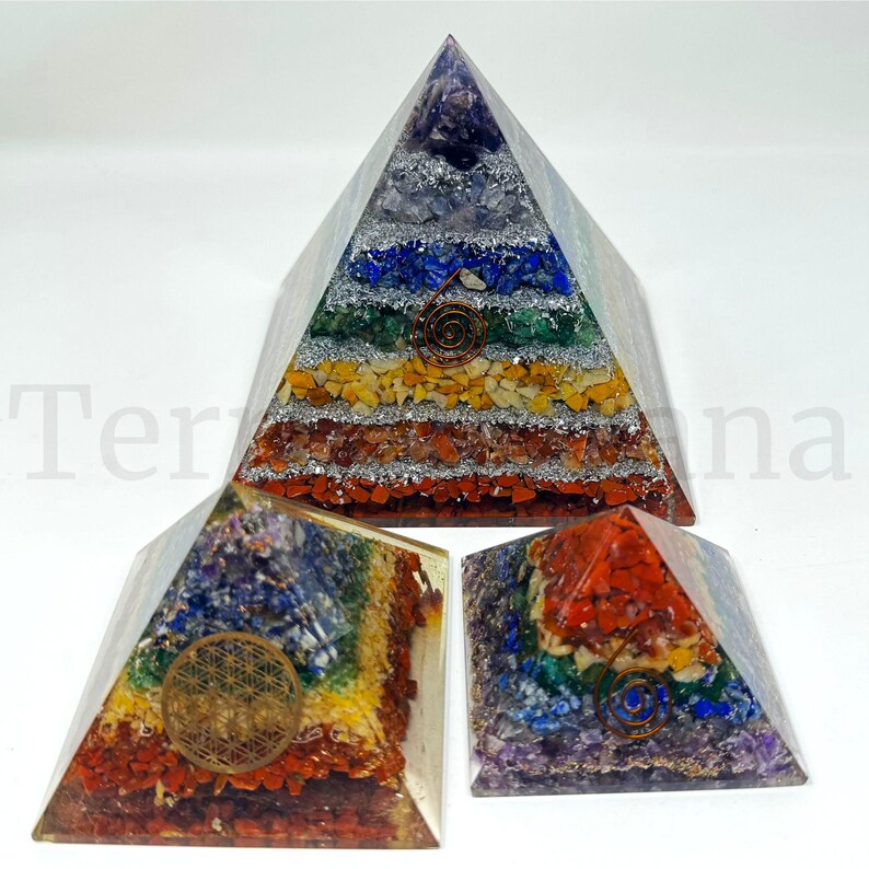 May include: Three orgone pyramids in varying sizes, showcasing a layered design with colorful gemstones and a copper coil or sacred geometry symbol. The pyramids feature a rainbow of colors, including purple, blue, green, yellow, orange, and red.