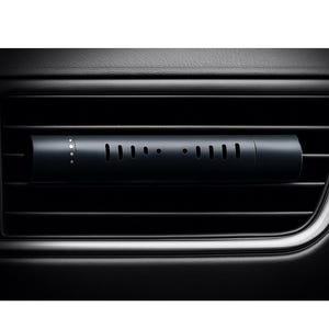 May include: A dark grey car air freshener is inserted into a black air vent. The cylindrical freshener has a series of small holes and dots along its surface. The air vent is part of a black dashboard.