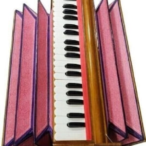 May include: A wooden harmonium musical instrument featuring a central keyboard with white and black keys, flanked by expandable bellows covered in textured pink fabric with purple trim, and a silver metal handle attached to the front base.