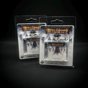 May include: Two packaged keychains featuring the "Pirates of the Caribbean: At World's End" soundtrack. Each package has a clear plastic front, displaying the CD-sized keychain with the movie's artwork and text. The packaging includes the text "Original Motion Picture Soundtrack".