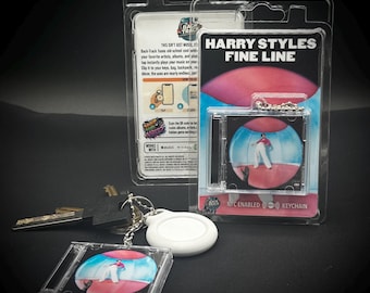 May include: A keychain featuring a miniature CD case with the album art from Harry Styles' "Fine Line." The keychain is in a clear plastic case, with a silver chain and a white tag. The packaging reads "NFC ENABLED KEYCHAIN."