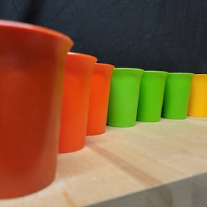 May include: A row of colorful plastic cups in orange and green. The cups are lined up on a wooden surface.