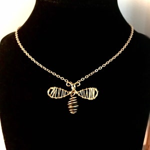May include: A gold chain necklace with a wire-wrapped bee pendant. The bee is made of gold wire and has a black bead for its body.
