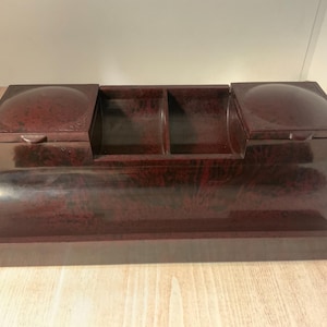 May include: A dark red, rectangular, vintage-style box with three compartments. The box has a curved, rounded base and two hinged lids.