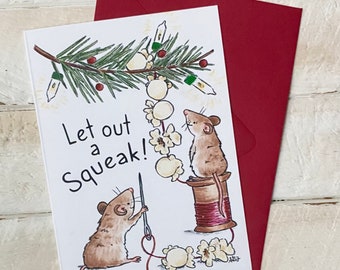 May include: A Christmas card featuring two mice decorating a popcorn garland. The card has the text "Let out a squeak!" on it.