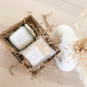 May include: A gift box filled with brown crinkle paper contains a white candle with the text "Cornish Escape" and a white soap bar with the text "Sundays in Spitios".
