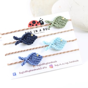 Könnte beinhalten: Vier handgefertigte Freundschaftsarmbänder mit Fischmotiven in Grün, Blau, Hellblau und Dunkelblau. Die Armbänder befinden sich auf einer weißen Karte mit dem Text "Bug in a Rug Handmade Crafts" und einem Marienkäfer-Logo.