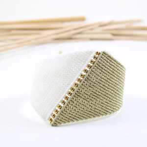 Può includere: Un braccialetto intrecciato bianco e beige con perline dorate sul bordo.