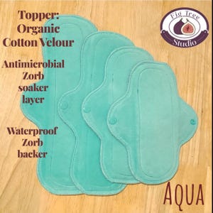 May include: Aqua-colored reusable cloth pads. The pads are made with organic cotton velour, antimicrobial Zorb soaker layer, and a waterproof Zorb backer. The image includes text that reads "Topper: Organic Cotton Velour, Antimicrobial Zorb soaker layer, Waterproof Zorb backer" and "AQUA".