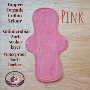 May include: A pink reusable menstrual pad with the word "PINK" in pink script. The pad is made of organic cotton velour, an antimicrobial Zorb soaker layer, and a waterproof Zorb backer. The Fig Tree Studio logo is in the lower left corner.