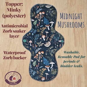 May include: Reusable cloth menstrual pad with a dark blue background and a pattern of mushrooms and foliage. The pad has a minky polyester topper, an antimicrobial Zorb soaker layer, and a waterproof Zorb backer. The text "MIDNIGHT MUSHROOMS" is visible.