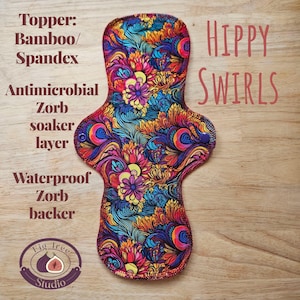 May include: A reusable menstrual pad with a vibrant floral pattern in shades of blue, purple, yellow, and red. The pad features the text "HIPPY SWIRLS" and product details. The pad is made with bamboo/spandex, a Zorb soaker layer, and a waterproof Zorb backer.