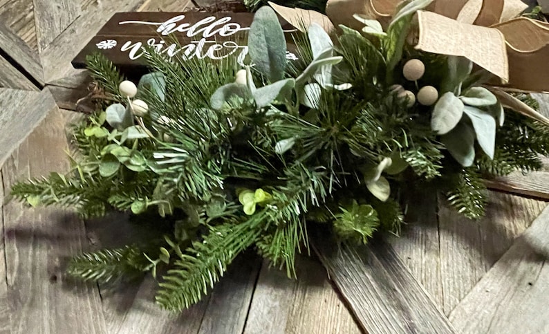 May include: A green and white winter wreath with a wooden sign that says "hello winter".