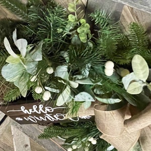 May include: A green and white Christmas wreath with a burlap bow and a wooden sign that says "hello winter".