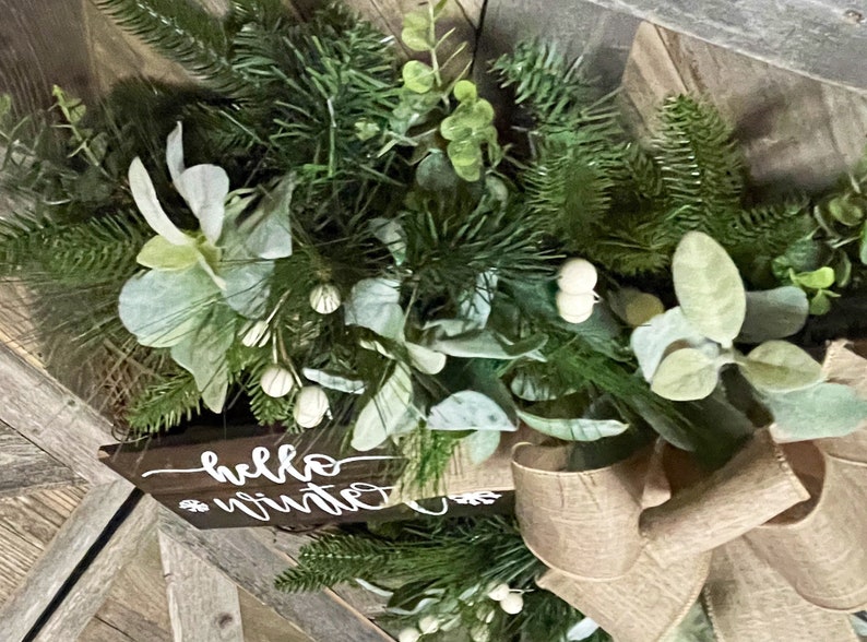 May include: A green and white Christmas wreath with a burlap bow and a wooden sign that says "hello winter".