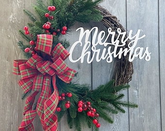 May include: A Christmas wreath with a grapevine base, adorned with evergreen branches, red berries, and a plaid bow. The white script text reads "Merry Christmas". A festive holiday decoration.