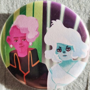 Może przedstawiać: Okrągły guzik z kolorowym wzorem przedstawiającym dwie postacie z kreskówek. Postać po lewej stronie ma różową skórę, różowe włosy i nosi czarną kurtkę z pomarańczowymi akcentami. Postać po prawej stronie ma niebieską skórę, białe włosy i nosi białą sukienkę.