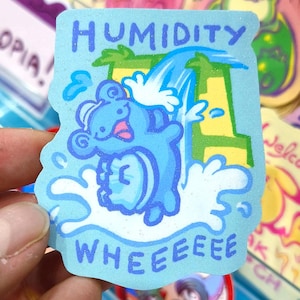 Könnte beinhalten: Hellblauer Aufkleber mit dem Wort „HUMIDITY“ oben und „WHEEEEE“ unten. Der Aufkleber zeigt eine Zeichentrickfigur in einem Wasserfall. Die Figur ist blau mit einer rosa Zunge und ist von Wasser umgeben.