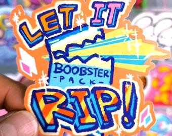 Könnte beinhalten: Ein farbenfroher Aufkleber mit den Worten "LET IT" in Orange und Blau und "RIP!" in Orange und Blau. Der Text "BOOBSTER PACK" befindet sich in einer blauen Box. Der Aufkleber hat einen leuchtend orangefarbenen Hintergrund mit Sternen.