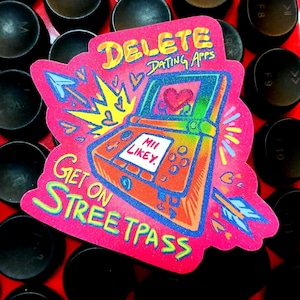 May include: A pink sticker with the text "DELETE DATING APPS" and "GET ON STREETPASS". The sticker features a colorful illustration of a handheld gaming device with a heart on the screen and an arrow.