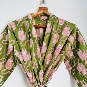 Peut inclure: Une robe à motif vert et rose avec une bordure blanche. La robe a une ceinture à nouer et des manches longues.